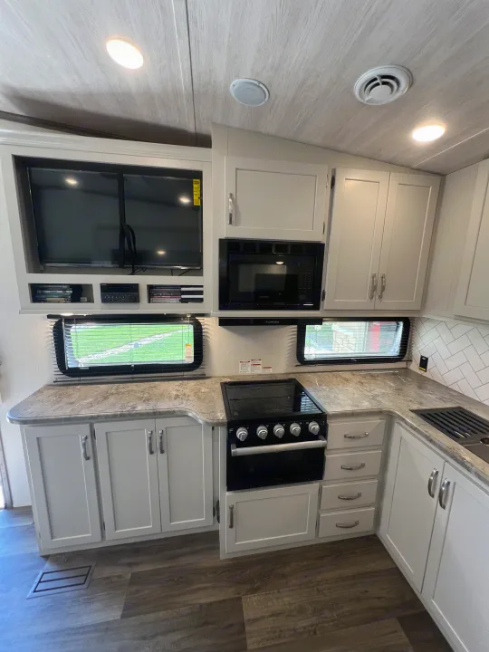 Inside an RV rental: a bright kitchen with white cabinetry, a microwave, stove, and TV. Ideal for comfortable road trips.. Keystone RV Cougar 2023