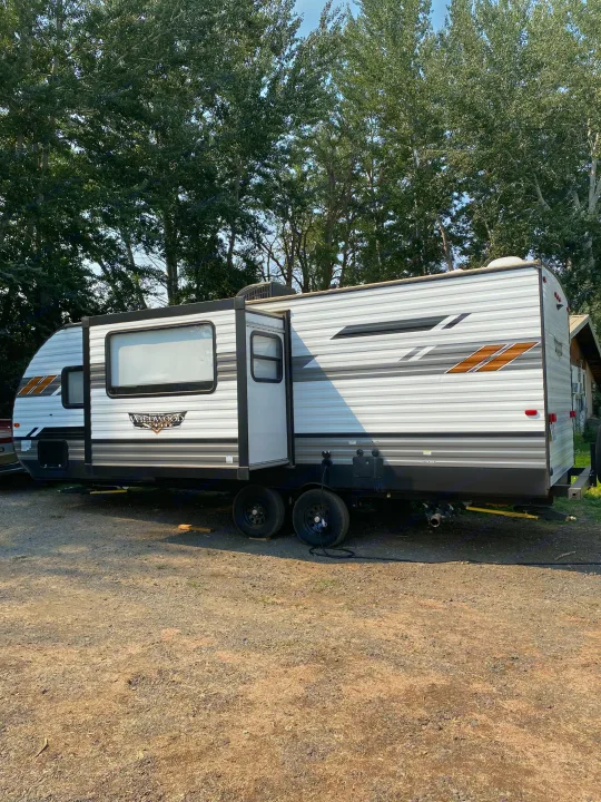Forest River Wildwood X-Lite travel trailer, an ideal rv rental. Parked on gravel, surrounded by trees for a serene camp.. Forest River Wildwood X-Lite 2022