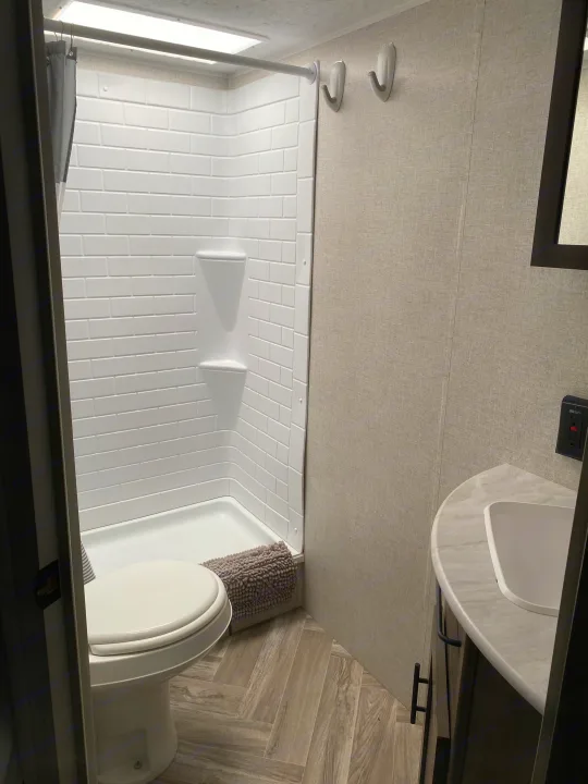 Modern RV rental bathroom with shower, toilet, and sink, featuring subway tile and wood-look flooring.. Forest River Wildwood X-Lite 2022