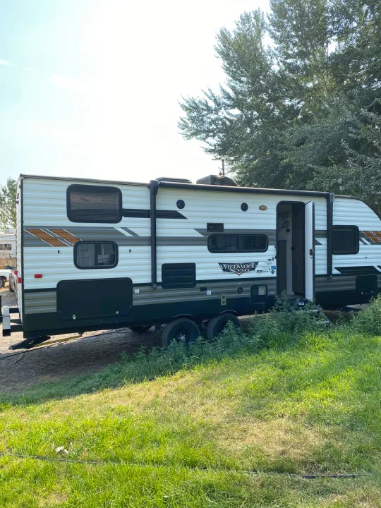 White & dark grey Wildwood X-Lite travel trailer (camper) parked on grass. Ideal for an RV rental.. Forest River Wildwood X-Lite 2022