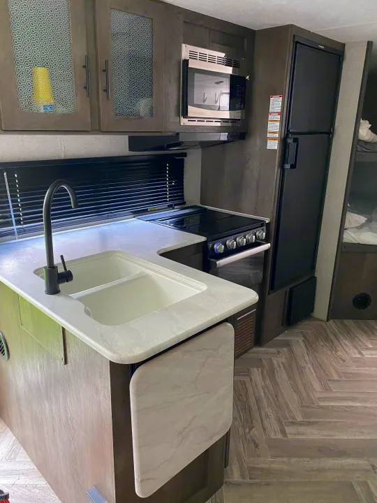RV rental kitchen featuring a sink, stove, microwave, refrigerator, and stylish counters with herringbone flooring.. Forest River Wildwood X-Lite 2022