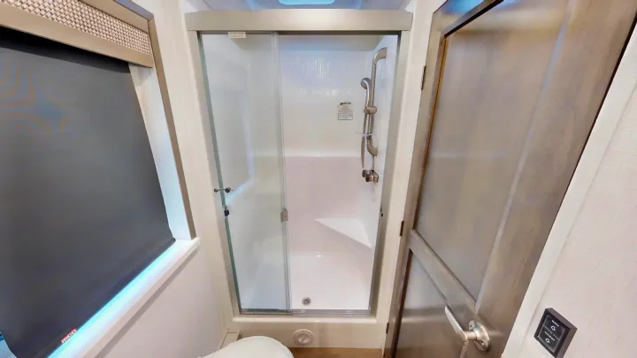 Compact RV rental bathroom: modern shower stall, window with shade, and interior door with light controls.. Georgetown GT7 2022
