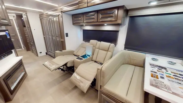 Modern RV rental living space featuring beige recliners, entertainment center, and extensive cabinetry for a comfortable journey.. Georgetown GT7 2022