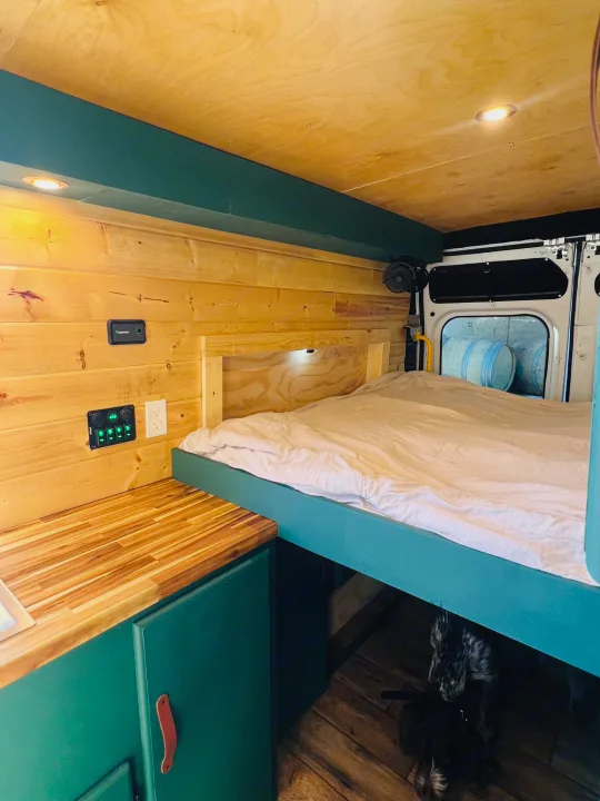 Cozy RV rental interior featuring wooden walls, a comfy bed, kitchenette, and a dog napping below.. Dodge ProMaster 2500 2018