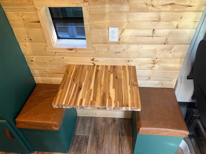 This RV rental's cozy dinette features light wood walls, a window, a butcher block table, and brown cushioned benches.. Dodge ProMaster 2500 2018