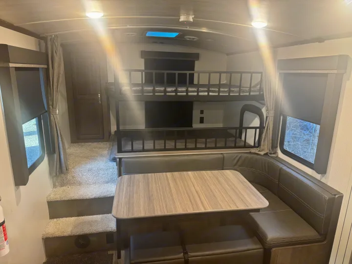 Spacious RV rental interior featuring double bunk beds, a U-shaped dinette, and carpeted stairs.. Keystone RV Cougar 2022