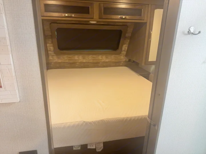 Step into this compact RV rental bedroom, featuring a new mattress, wood-paneled headboard, and overhead cabinets.. Keystone RV Cougar 2022