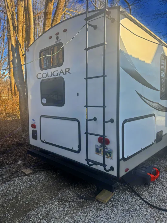 Rear of a white Keystone Cougar RV rental, parked. Ladder, windows, and external utilities visible.. Keystone RV Cougar 2022