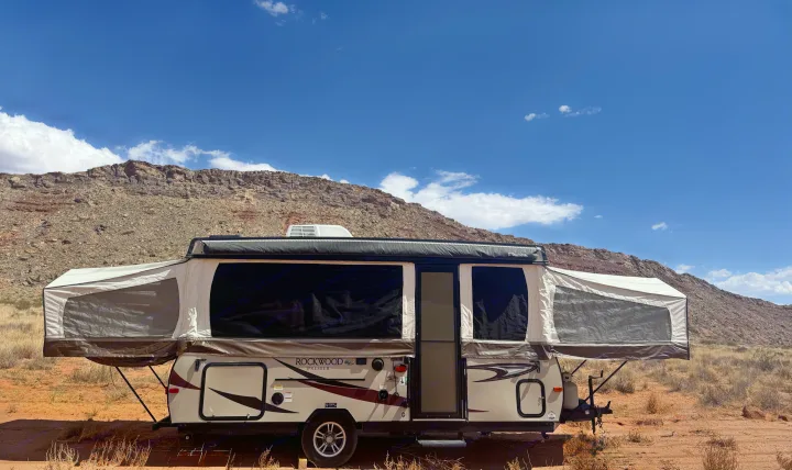 Explore the outdoors! This tan pop-up RV rental is set up for desert camping, framed by rocky mountains & blue sky.. Forest River Rockwood Premier 2017