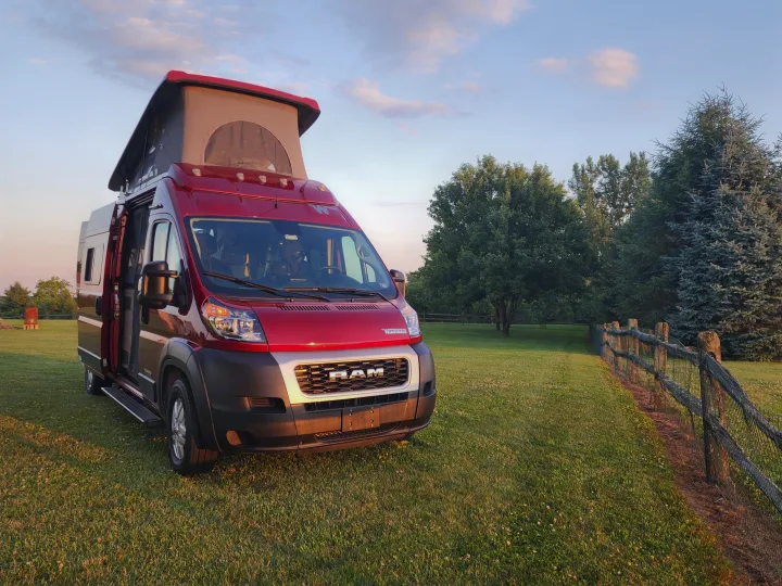 Red Winnebago camper van RV rental, pop-top open, ready for adventure on a grassy field at golden hour.. Winnebago Solis 2022