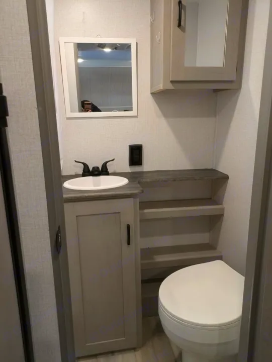 RV rental bathroom with a gray vanity, white sink, mirror, open shelves, and toilet. Space-saving and practical interior.. Forest River Coachmen Clipper 2024