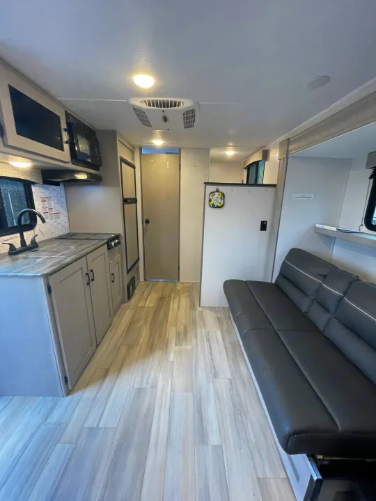 Spacious RV rental interior featuring a modern kitchenette, comfortable black sofa, and light wood-look flooring.. Forest River Coachmen Clipper 2024