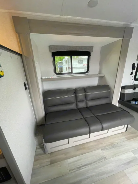Modern RV rental interior with a dark gray sofa, window, and light wood flooring. Comfortable living area.. Forest River Coachmen Clipper 2024