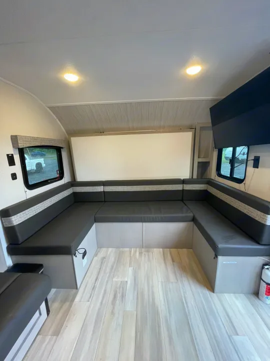 Inside a bright RV rental: U-shaped dinette with dark cushions, light wood floor, and windows. Converts to a bed.. Forest River Coachmen Clipper 2024