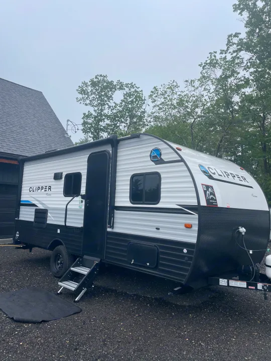 A gray and white Clipper travel trailer is parked with steps down and awning out, ideal for an RV rental camping adventure.. Forest River Coachmen Clipper 2024