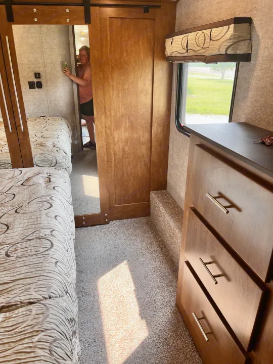 An RV rental bedroom with two comfy beds, a mirrored closet door, and a wooden dresser by the window.. Forest River Sabre 2019