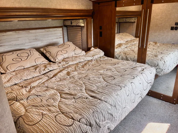 Cozy RV rental bedroom features a cream, patterned bed and pillows. A large mirrored wardrobe reflects the comfortable space.. Forest River Sabre 2019