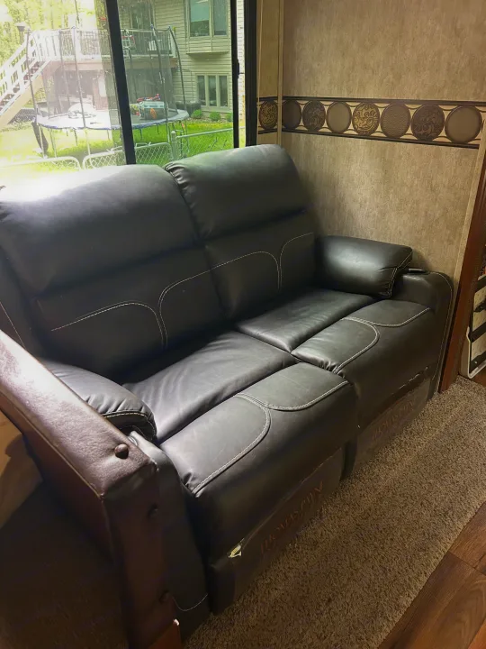 Black leather Thomas Payne RV reclining sofa in an RV rental, with a backyard view out the window.. Keystone RV Passport Grand Touring 2015
