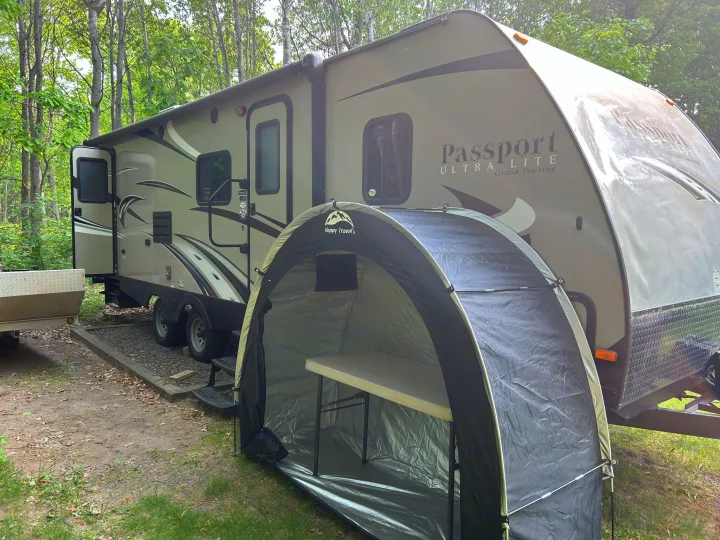 This RV rental, a Passport Ultra Lite travel trailer, is set up at a scenic campground with a handy portable tent.. Keystone RV Passport Grand Touring 2015