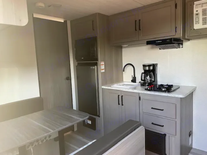 Modern RV rental interior featuring a compact kitchen with sink, stove, coffee maker, and microwave, plus a dinette.. Keystone RV Hideout Sport 2024