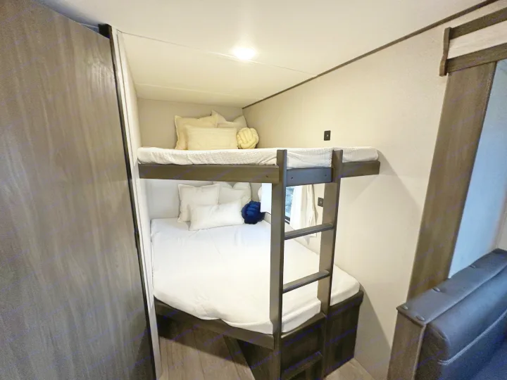 Cozy bunk beds in an RV rental, featuring white bedding, pillows, and a ladder in a compact space.. Forest River Grand River Comfortline 2021
