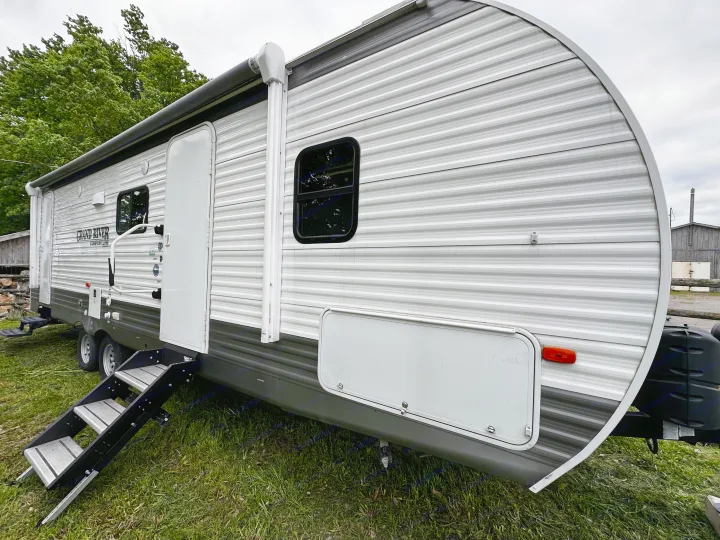 Grey and white travel trailer rv rental parked on grass, showing exterior steps, window, and awning. Perfect for outdoor adventures.. Forest River Grand River Comfortline 2021