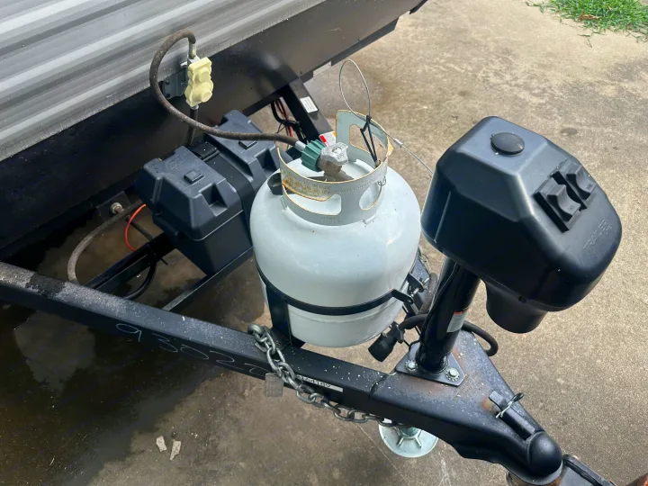 Front of an RV rental: white propane tank, black battery box, power tongue jack, and safety chains on the trailer hitch.. Coleman Lantern 17B 2024