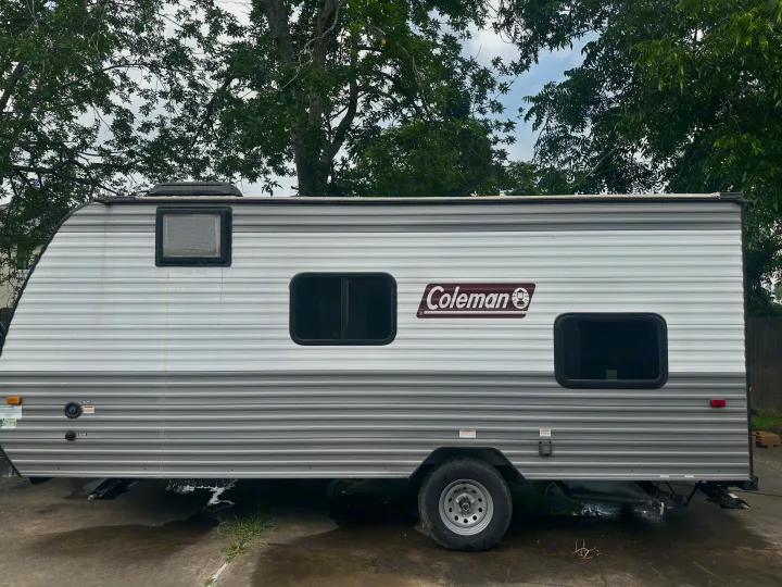 White and grey Coleman travel trailer, ideal for your next RV rental adventure. Parked under trees on concrete.. Coleman Lantern 17B 2024