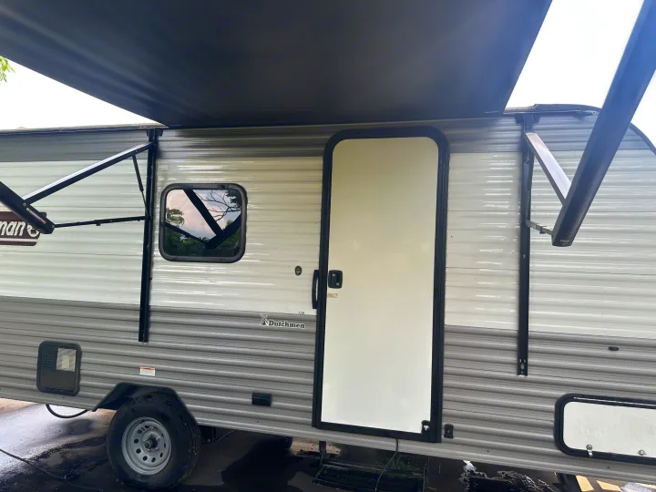 A gray and white travel trailer RV with its black awning extended, ready for adventure. Explore the open road with this RV rental!. Coleman Lantern 17B 2024