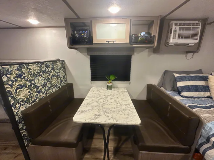 RV rental interior: a dinette with marble table, bunk beds (one floral, one striped), overhead cabinets, and AC unit.. Coleman Lantern 17B 2024