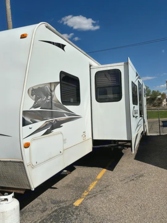 This white Cougar RV rental, with its side slide-out extended, is parked on asphalt under a blue sky.. Keystone RV Cougar 2008