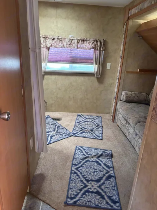 RV rental living area: Tan carpet, blue patterned rugs, patterned sofa, and a window. Typical camper interior view.. Keystone RV Cougar 2008