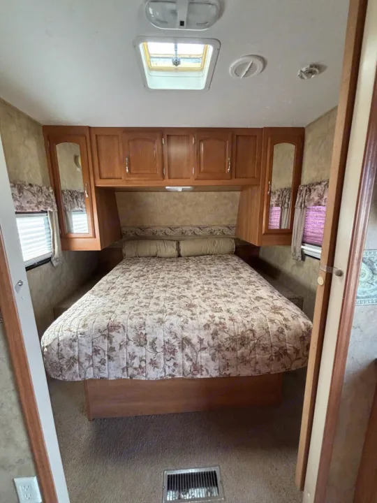 Cozy RV rental bedroom with floral bedding, ample wood storage, windows, and skylight for natural light.. Keystone RV Cougar 2008