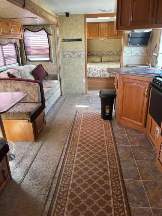 This RV rental interior showcases a living area with sofa & dining booth, a functional kitchen, and a private bedroom.. Keystone RV Cougar 2008