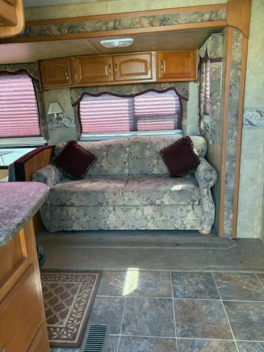 This RV rental's living area features a floral sofa, red blinds, and wood cabinets, offering a cozy, functional space for travel.. Keystone RV Cougar 2008