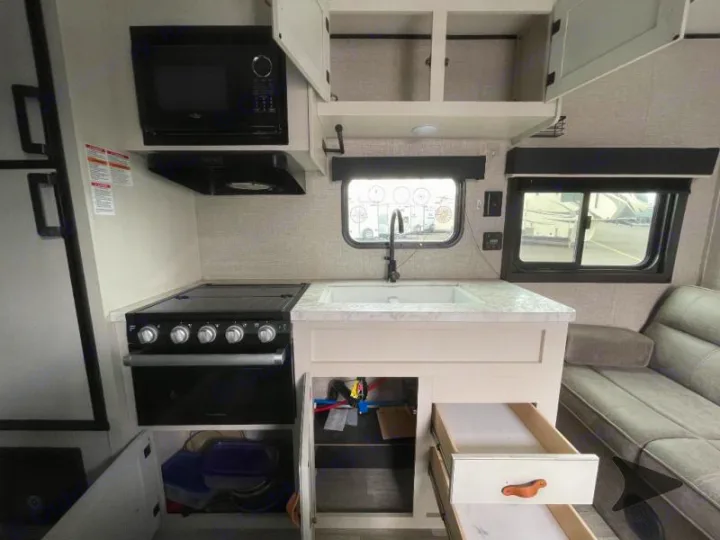 RV rental kitchen: microwave, stove, sink, and cabinets. Compact, modern interior for travel cooking.. Jayco Jay Flight SLX 2022