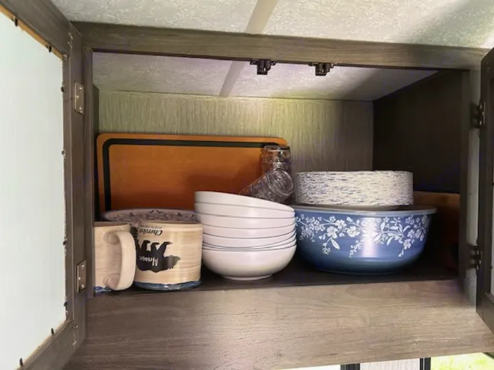 RV rental's cabinet, neatly stocked with kitchenware: bowls, mugs, plates, and a cutting board for your camping adventures.. Coachmen Pursuit 31bh 2023