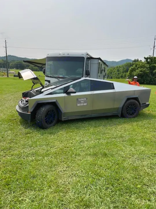 A Tesla Cybertruck with open hood on grass, promoting Southlake RV Park next to an RV. Perfect for RV rental vacations!. Coachmen Pursuit 31bh 2023