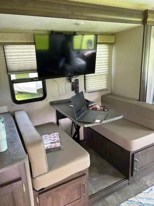 Spacious RV rental interior featuring a comfortable dinette, wall-mounted TV, and a laptop workspace for travel convenience.. Coachmen Pursuit 31bh 2023