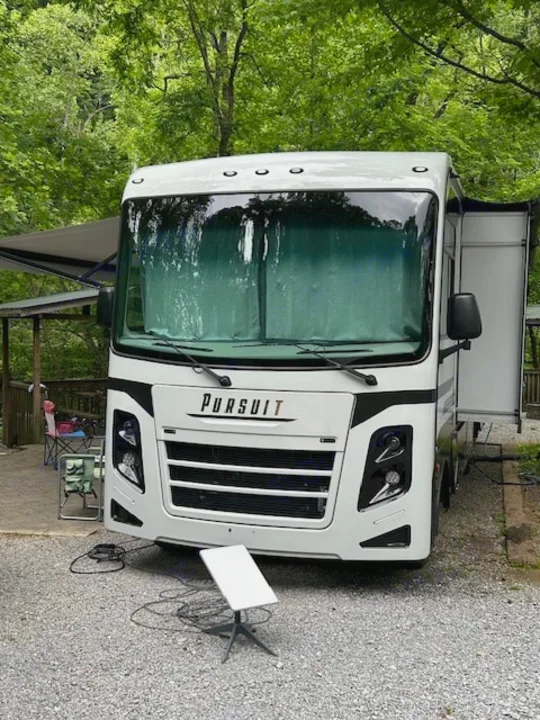 Modern white RV rental, a Pursuit motorhome, set up at a leafy campground with Starlink dish for connectivity.. Coachmen Pursuit 31bh 2023