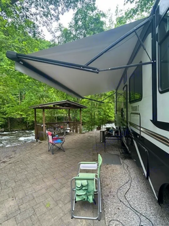 Enjoying a scenic RV rental campsite by the river, complete with an extended awning & patio setup for ultimate relaxation.. Coachmen Pursuit 31bh 2023