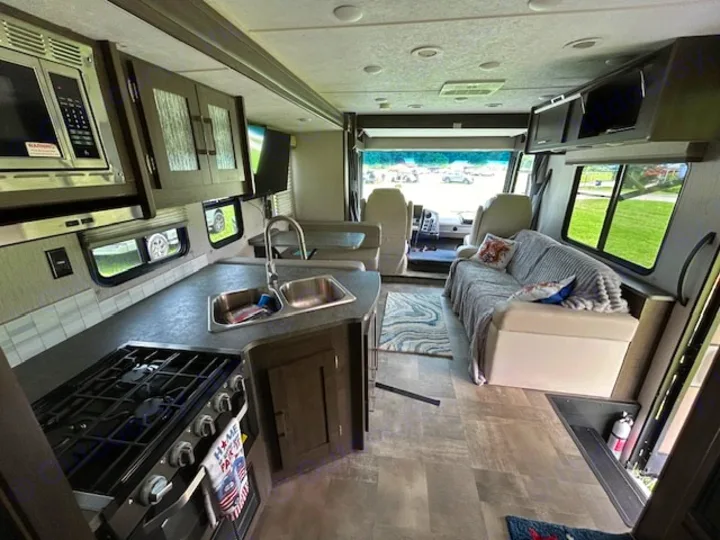 Spacious RV rental interior featuring a full kitchen, comfortable living area with sofa, and driver's cabin view.. Coachmen Pursuit 31bh 2023