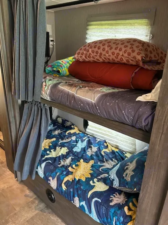 RV rental interior: two cozy bunk beds with space and dinosaur bedding, privacy curtains, and window blinds.. Coachmen Pursuit 31bh 2023