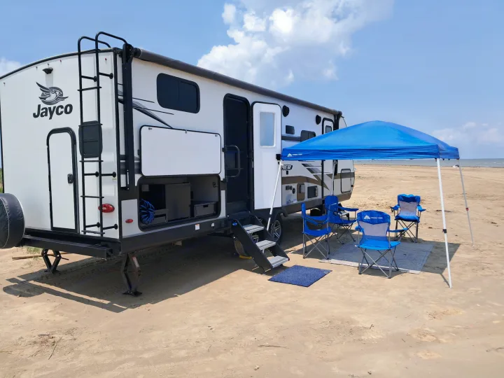 This RV rental is set up for a beach camping adventure, complete with chairs, a canopy, and ocean views.. Jayco Jay Feather 2022