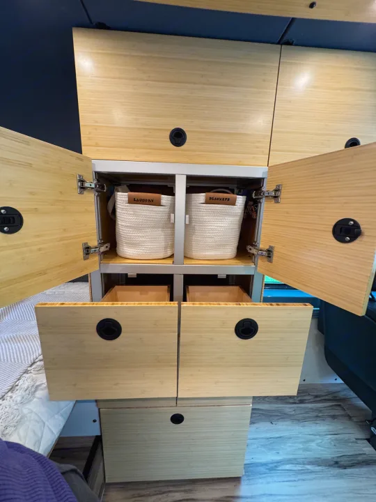 RV rental: Sleek bamboo-look storage in a camper van. Open cabinets reveal organized "Laundry" and "Blankets" baskets. Drawers below.. Mercedes-Benz Sprinter 2021