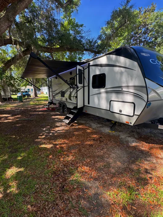 Spacious RV rental set up at a leafy campsite, featuring an extended awning and bright steps for easy access.. Keystone RV Cougar 2022