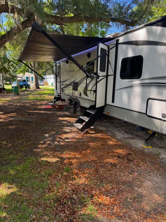 A white rv rental with awning extended, parked under mossy oak trees. Steps visible for easy access to this camping vehicle.. Keystone RV Cougar 2022