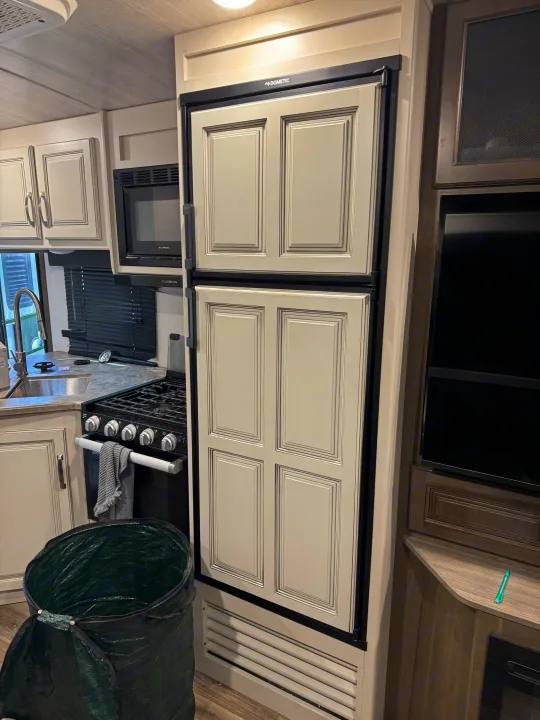 Modern RV rental kitchen featuring a large paneled refrigerator, stove, and microwave, creating a functional travel space.. Keystone RV Cougar 2022