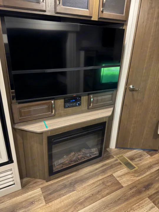 RV rental's modern interior showcases a large TV, integrated sound system, and electric fireplace, set on wood-look flooring.. Keystone RV Cougar 2022