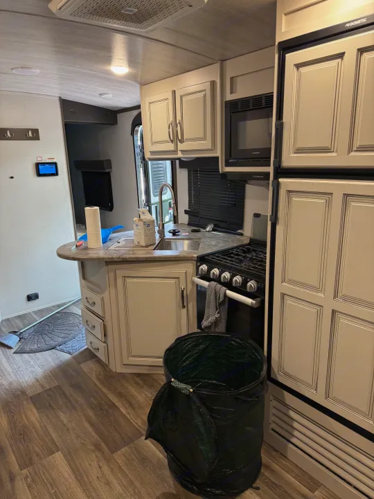This RV rental kitchen features a modern sink, stove, microwave, refrigerator, and wood-look flooring, ready for your trip.. Keystone RV Cougar 2022
